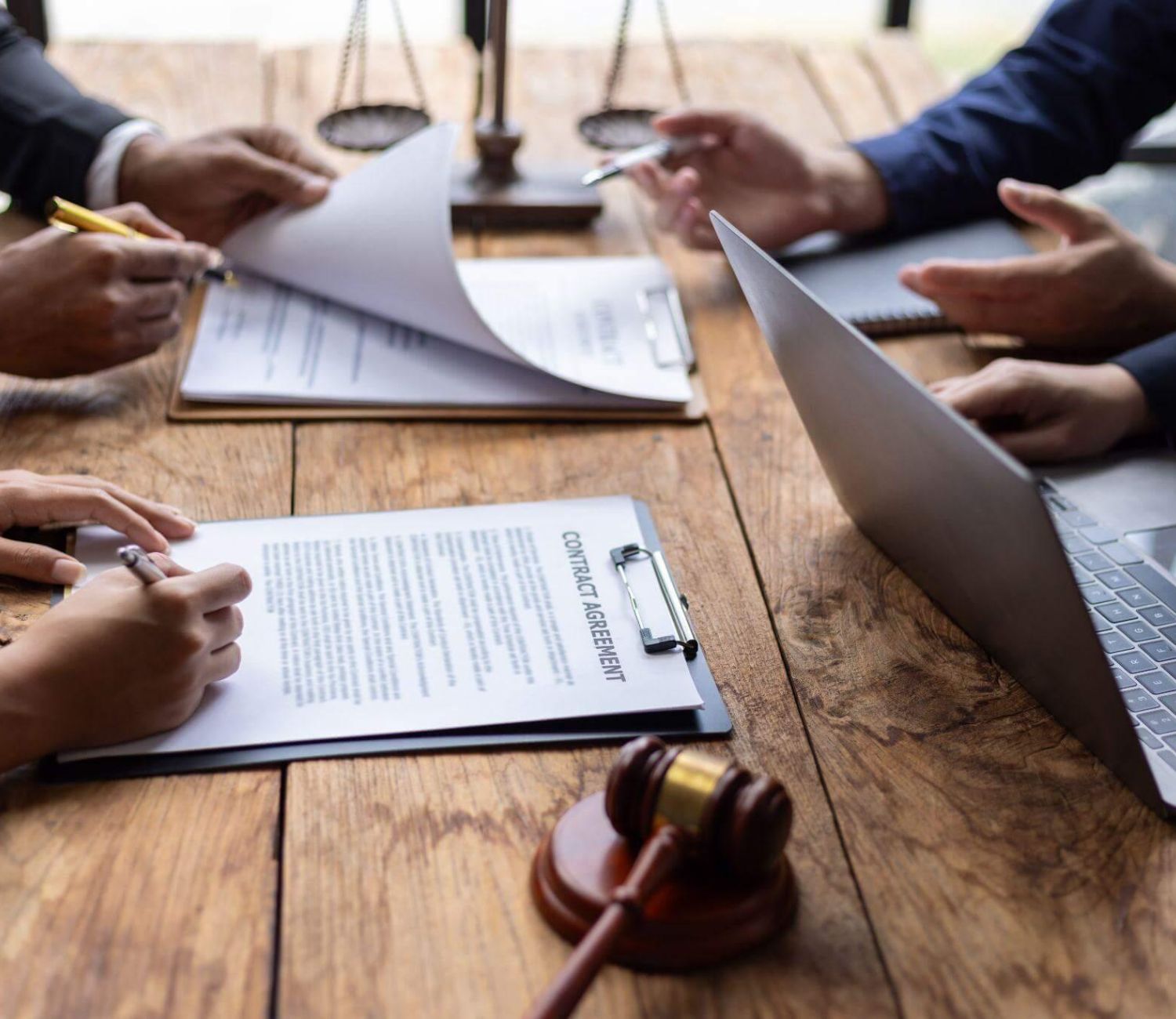 a group of people sitting around a wooden table and working with multiple documents and laptops