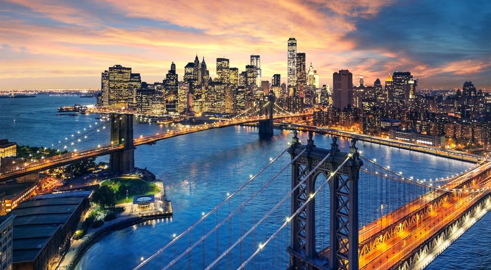 Aerial view of California City skyline at sunset with lit bridges and skyscrapers reflecting in the river.
