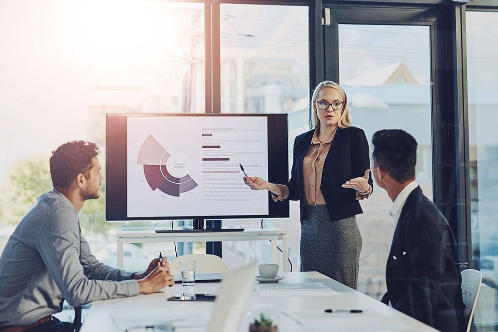 Business presentation in modern office with graphs on screen.