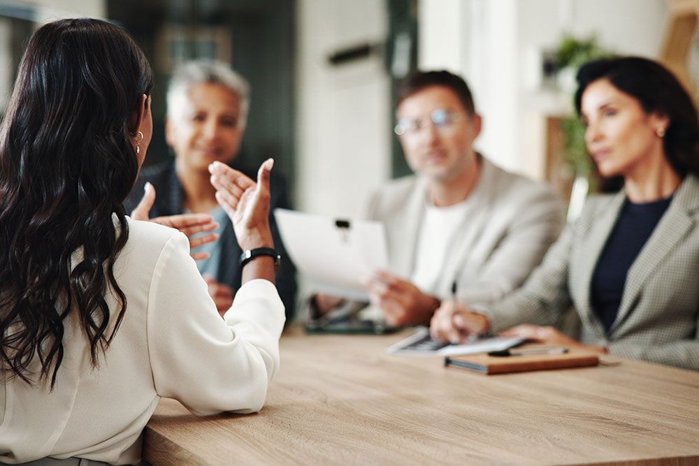 Woman in white shirt at meeting table discussing with three colleagues in office setting.