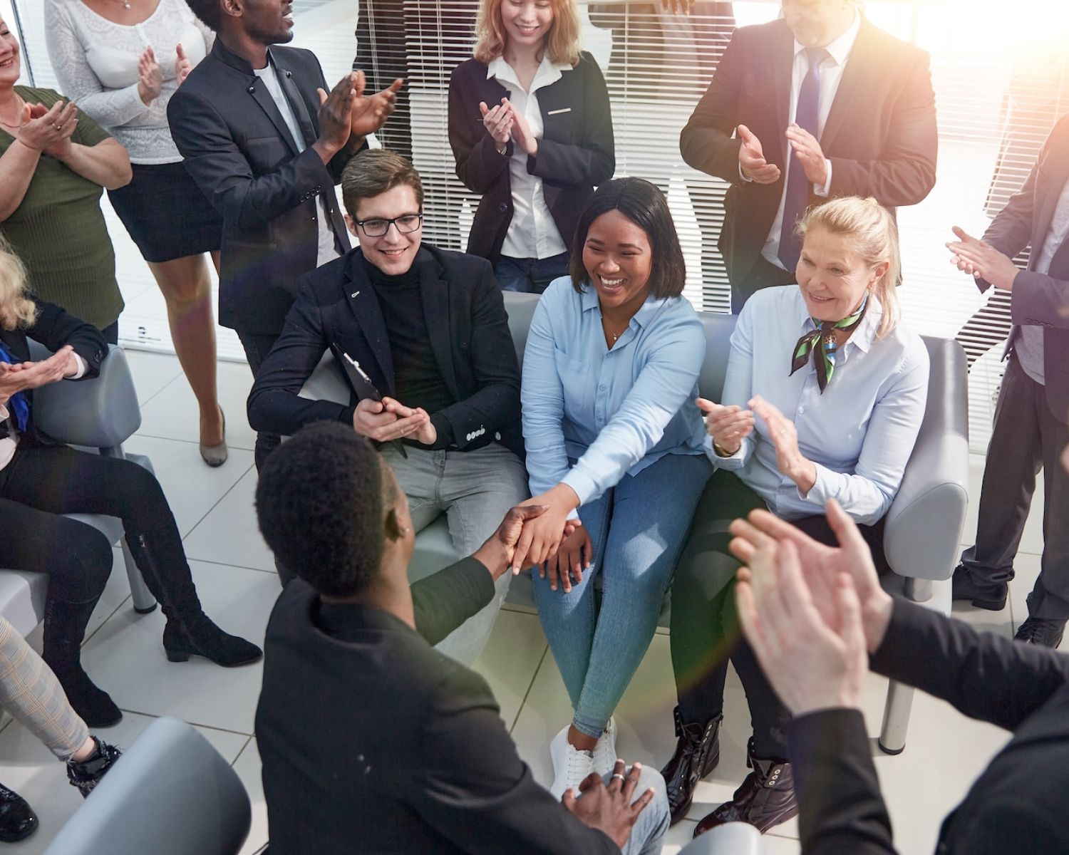 Diverse group of professionals clapping and shaking hands in a meeting, symbolizing teamwork and collaboration.
