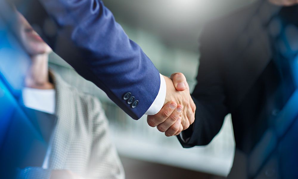 Business handshake between two professionals in suits, symbolizing partnership and agreement in a corporate setting.