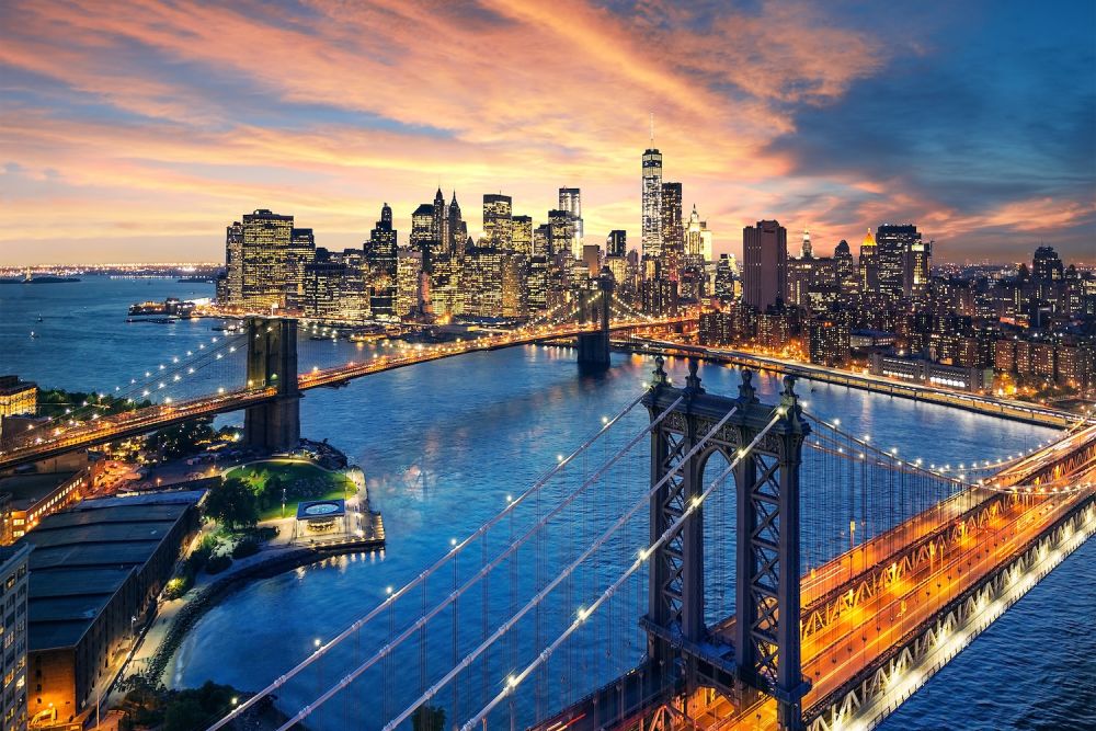 Aerial view of California City skyline at sunset with lit bridges and skyscrapers reflecting in the river.
