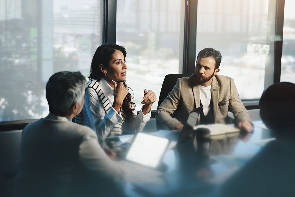Business meeting in a modern office with diverse professionals engaged in discussion around a conference table.