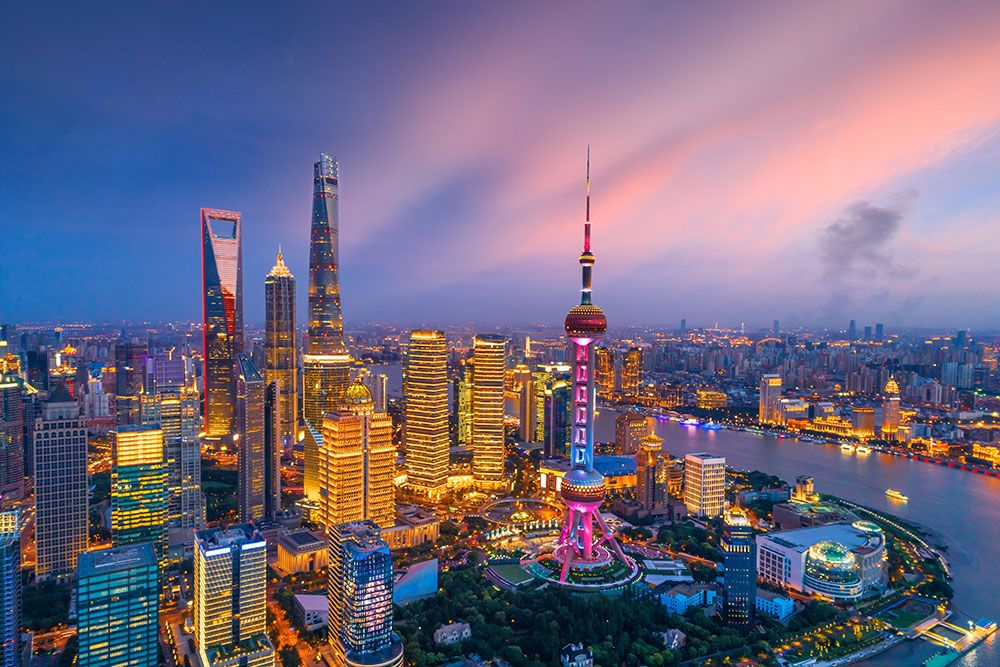 Shanghai cityscape at sunset with lit skyscrapers and the iconic Oriental Pearl Tower reflecting on the Huangpu River.