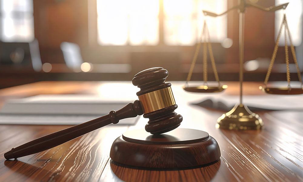 Wooden gavel on judge's table with scales of justice, symbolizing law and judgment in a courtroom setting.