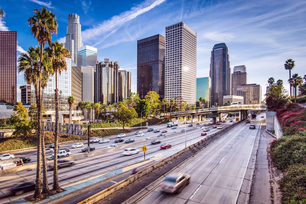 Bustling freeway with skyscrapers and palm trees under a clear blue sky in downtown Los Angeles.