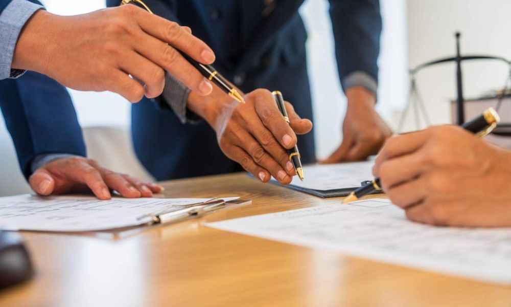 Business meeting with documents and pens on table, hands collaborating over contract details.