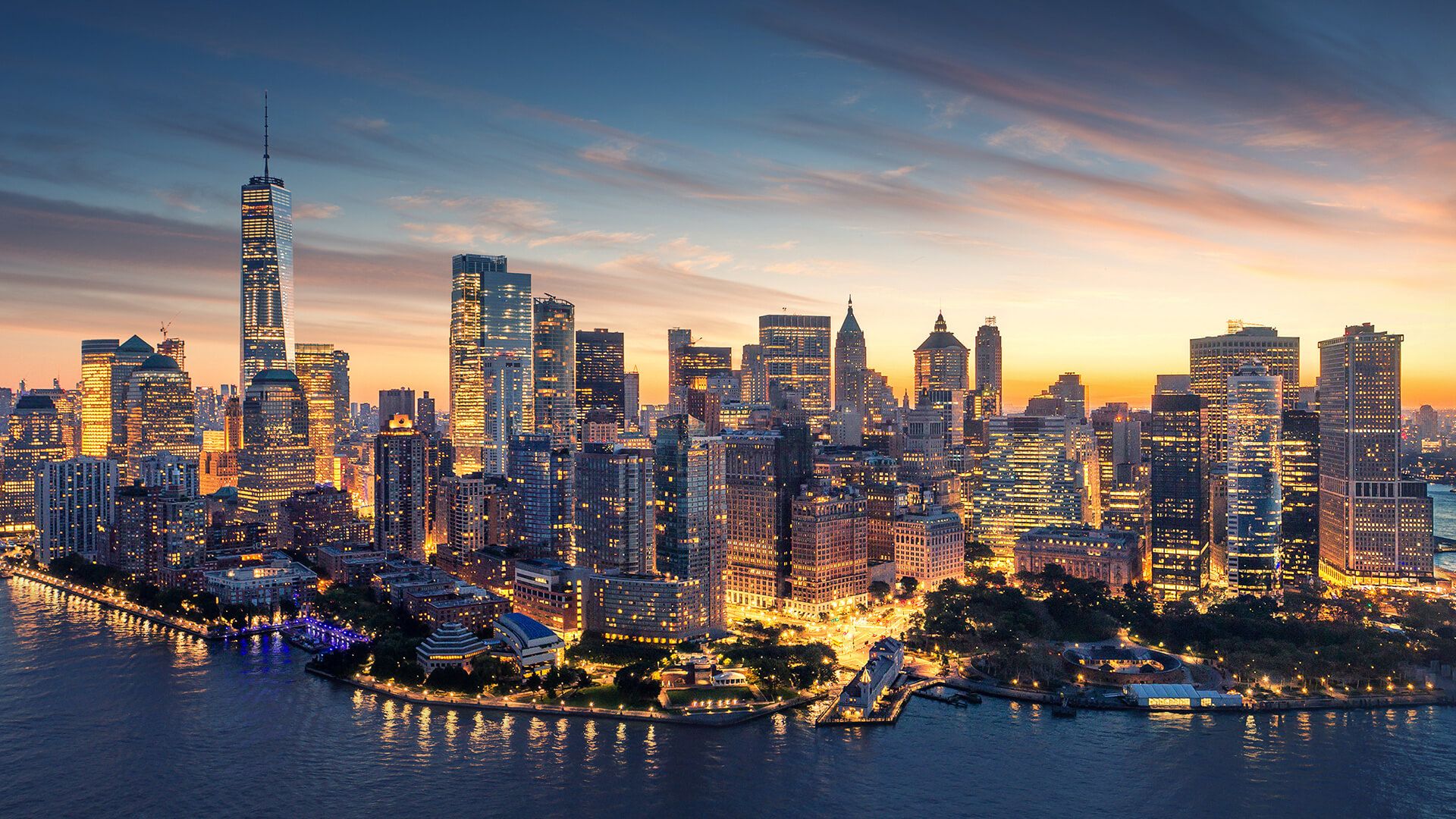 Aerial view of California City skyline at sunset, showcasing illuminated skyscrapers and waterfront reflections.