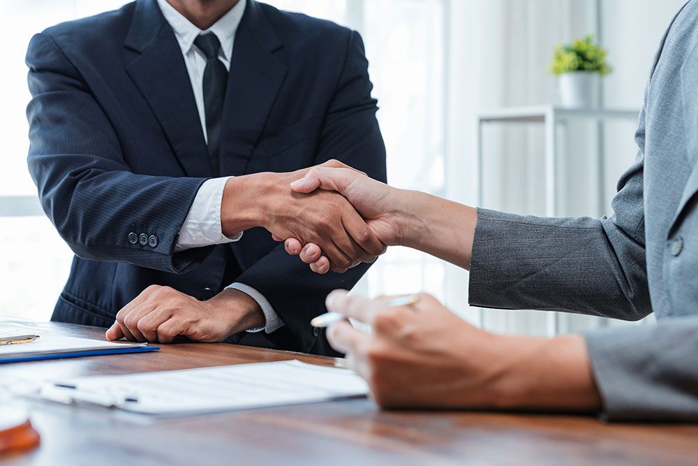 Business handshake between two professionals in suits at a wooden desk, symbolizing successful collaboration.