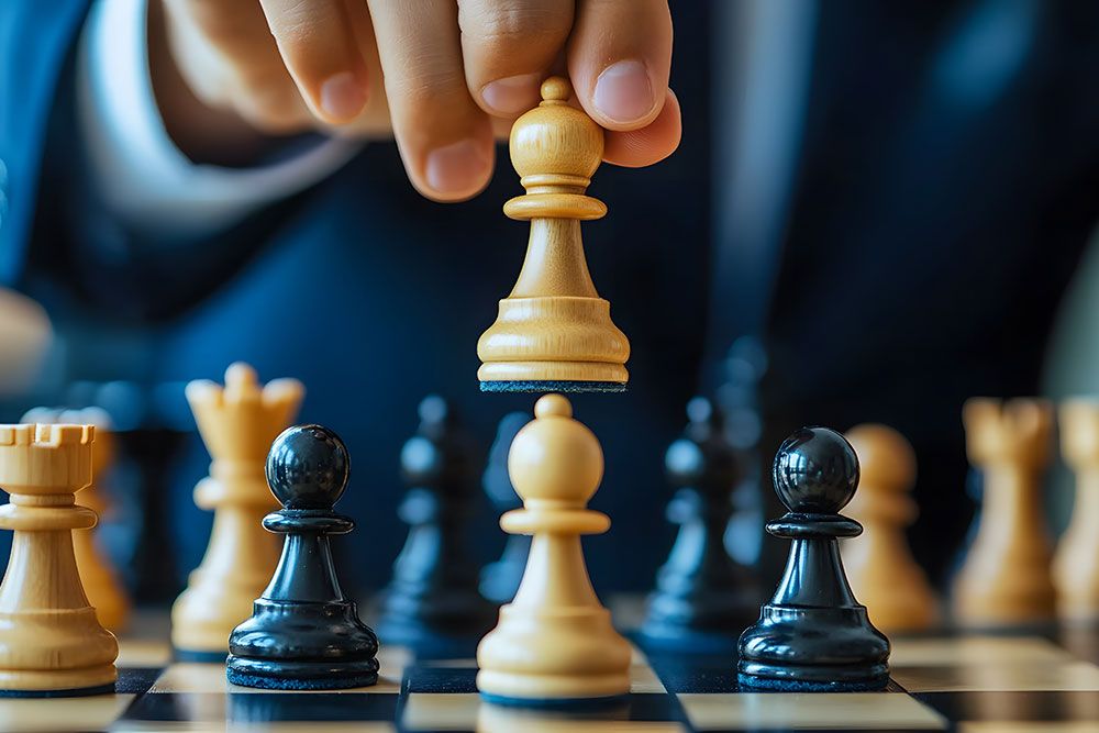 Person moving a white chess piece on a chessboard, symbolizing strategic thinking and decision-making in a game of chess.