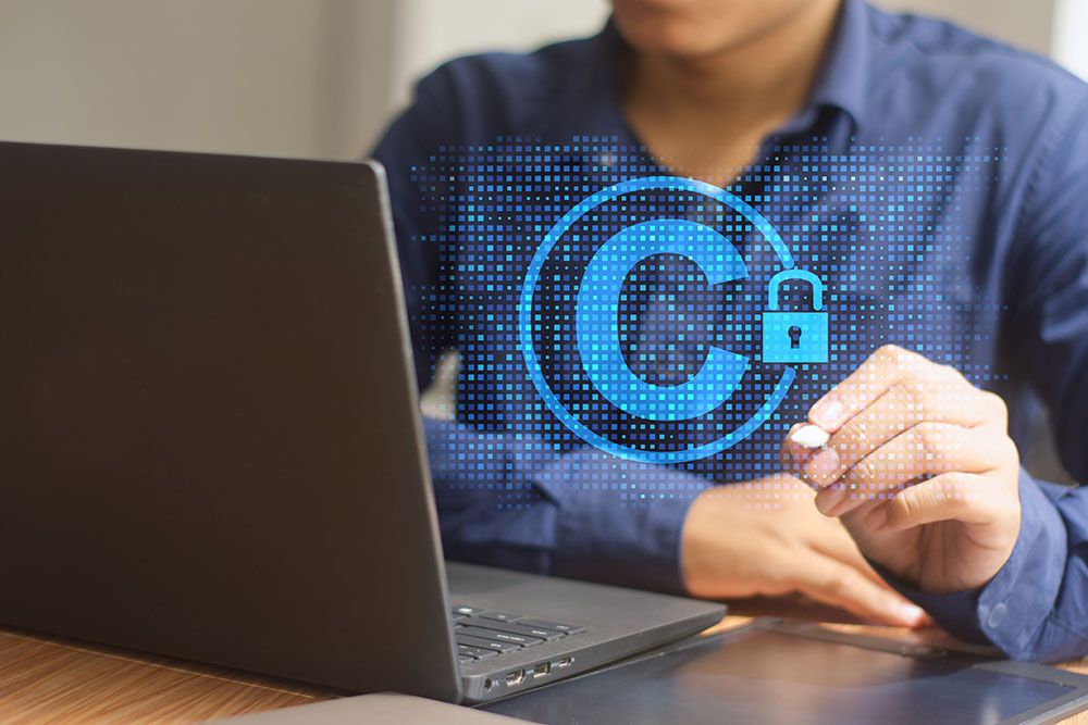 Person working on laptop with holographic copyright symbol and padlock, symbolizing digital content protection.
