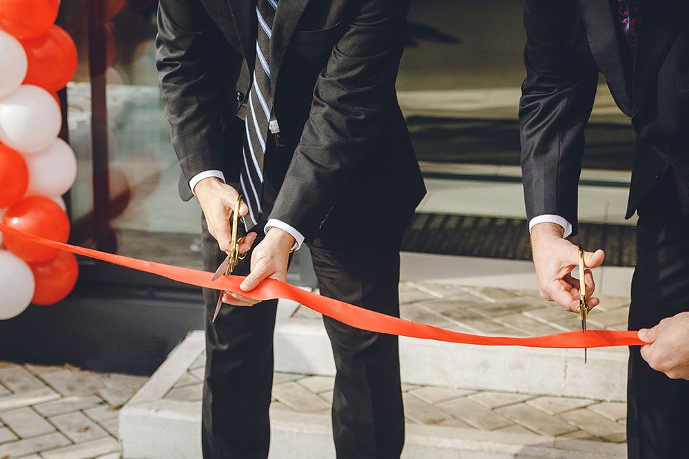 Businessmen cutting red ribbon at grand opening ceremony.