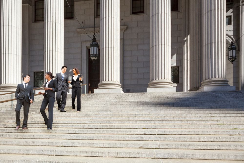 Business professionals walking down courthouse steps, discussing legal matters in formal attire.
