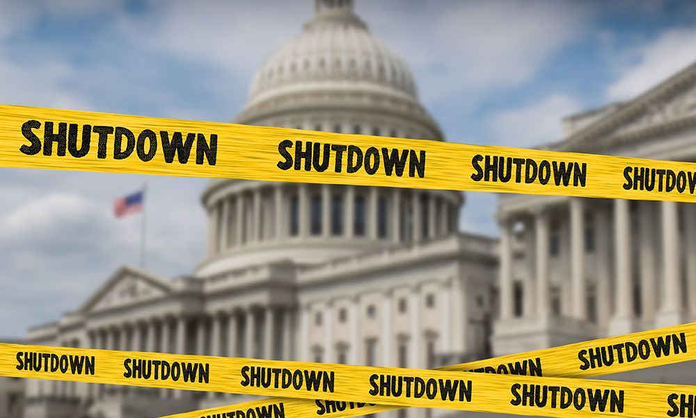 Yellow shutdown tape around blurred government building, symbolizing a governmental closure.