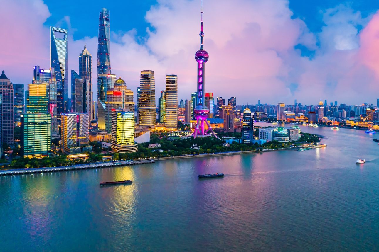 Shanghai skyline at sunset with illuminated skyscrapers and the Huangpu River reflecting vibrant city lights.