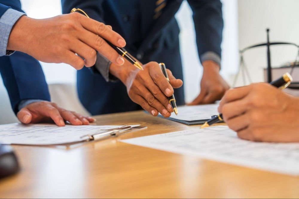Business meeting with documents and pens on table, hands collaborating over contract details.
