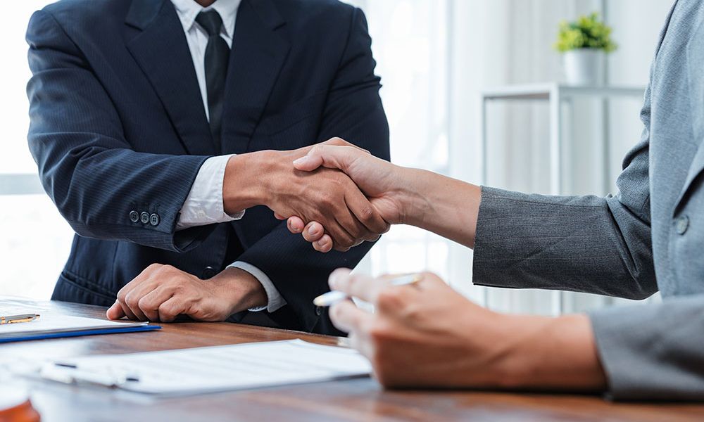 Business handshake between two professionals in suits at a wooden desk, symbolizing successful collaboration.