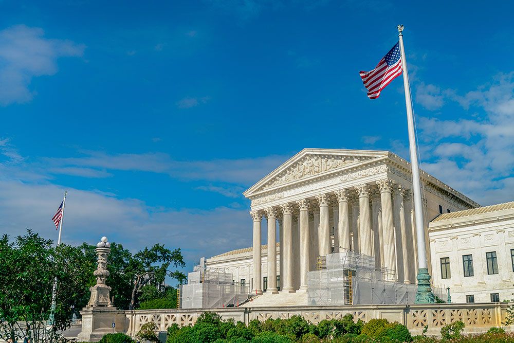 U.S. Supreme Court building with American flag under clear blue sky, showcasing neoclassical architecture.
