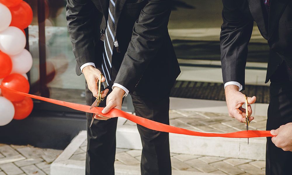 Businessmen cutting red ribbon at grand opening ceremony.