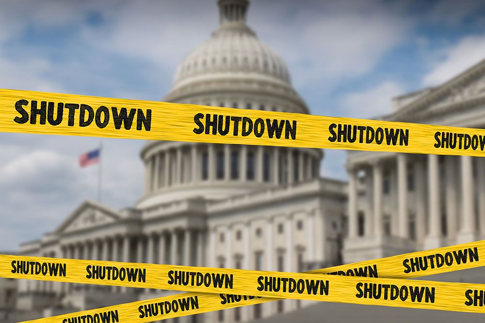 Yellow shutdown tape around blurred government building, symbolizing a governmental closure.