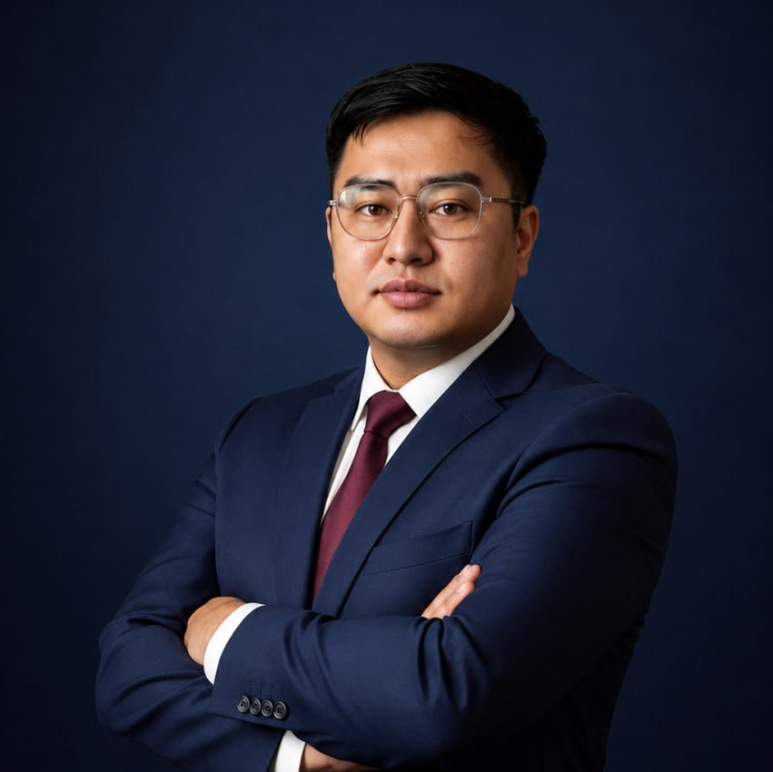 A person in a suit in an office setting, with a confident expression, facing forward.