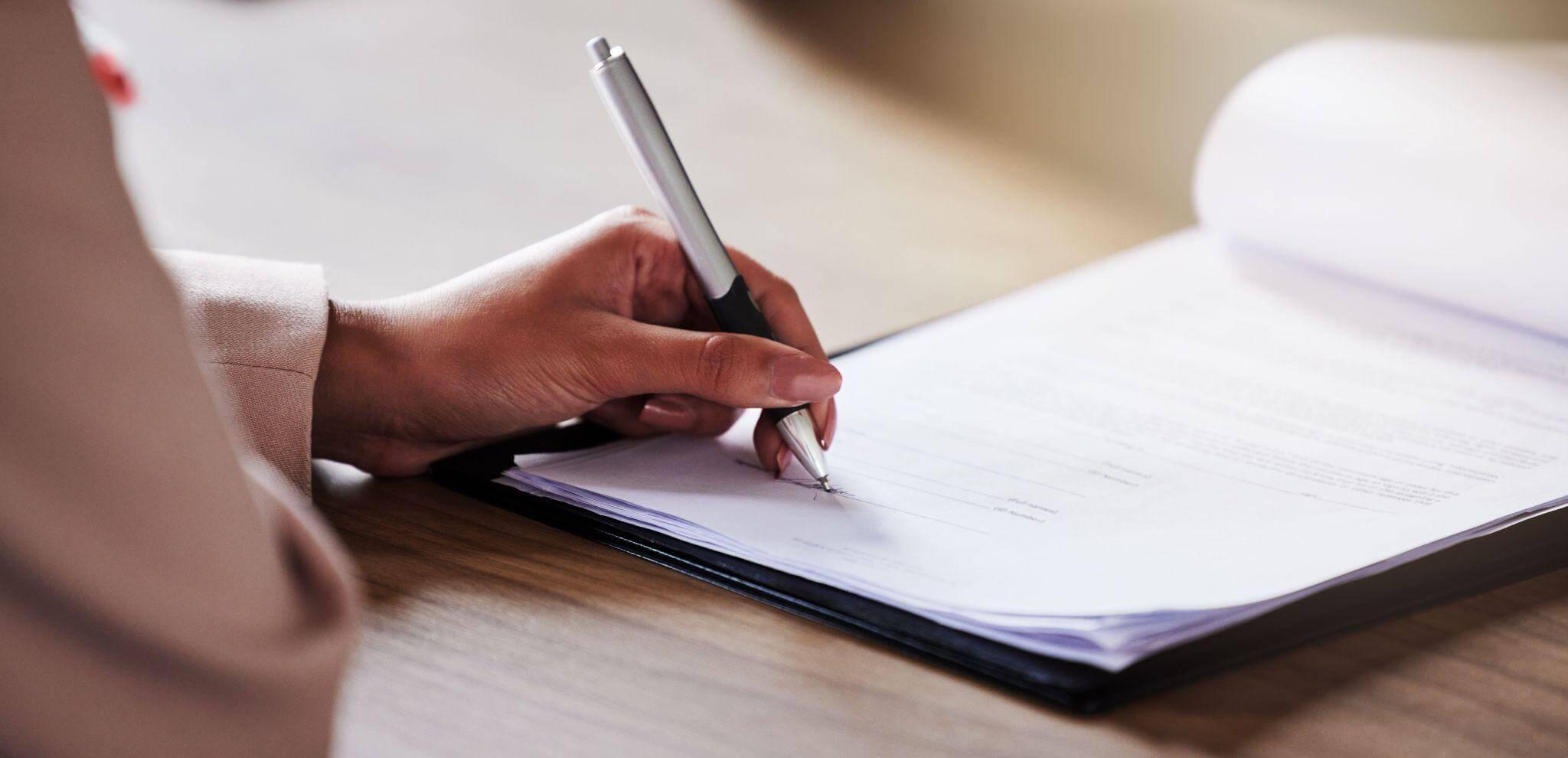 a person writing on a piece of paper with a pen; it looks like a legal document with multiple pages