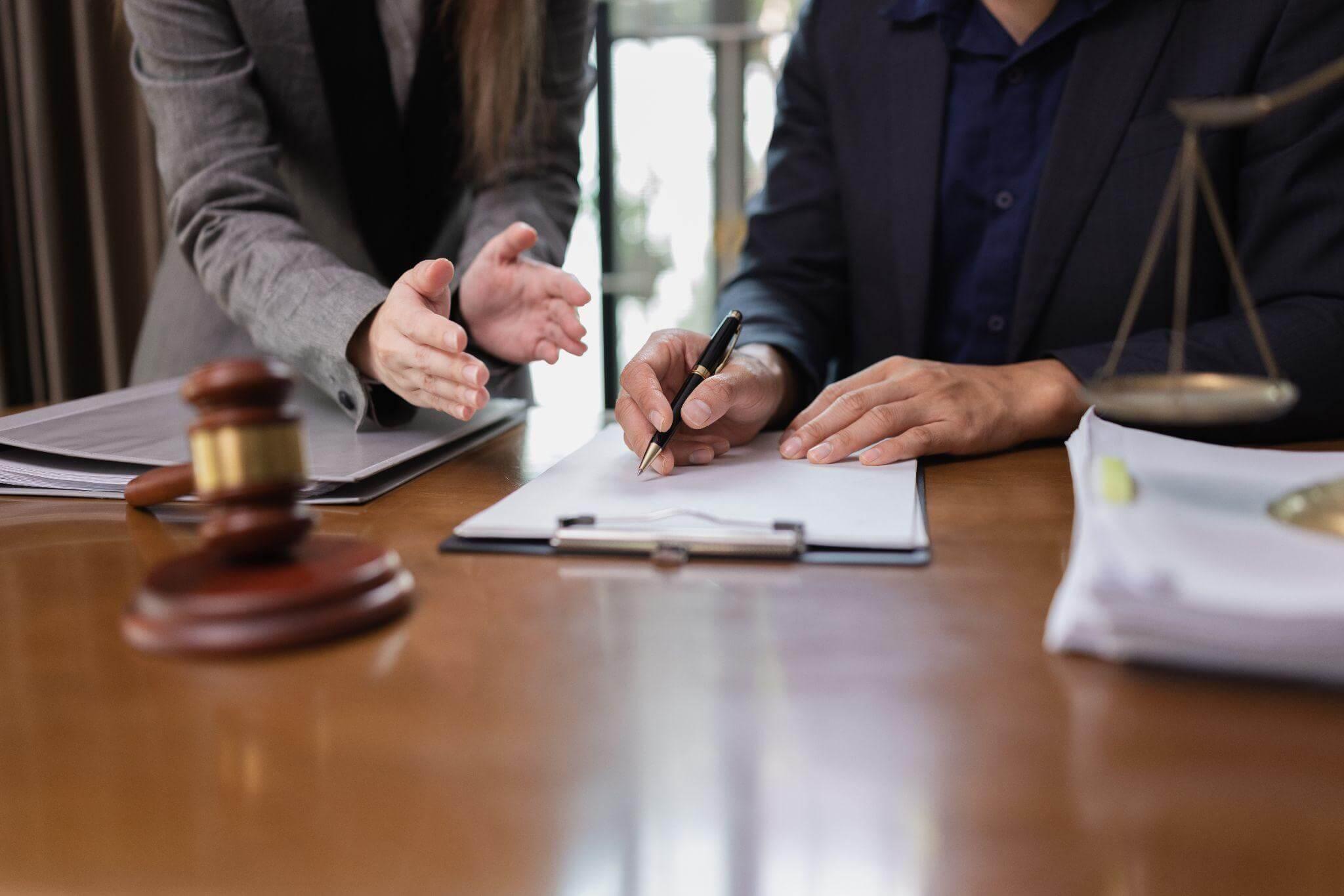 two people sitting at a table with a gavel; they are reviewing and signing documents