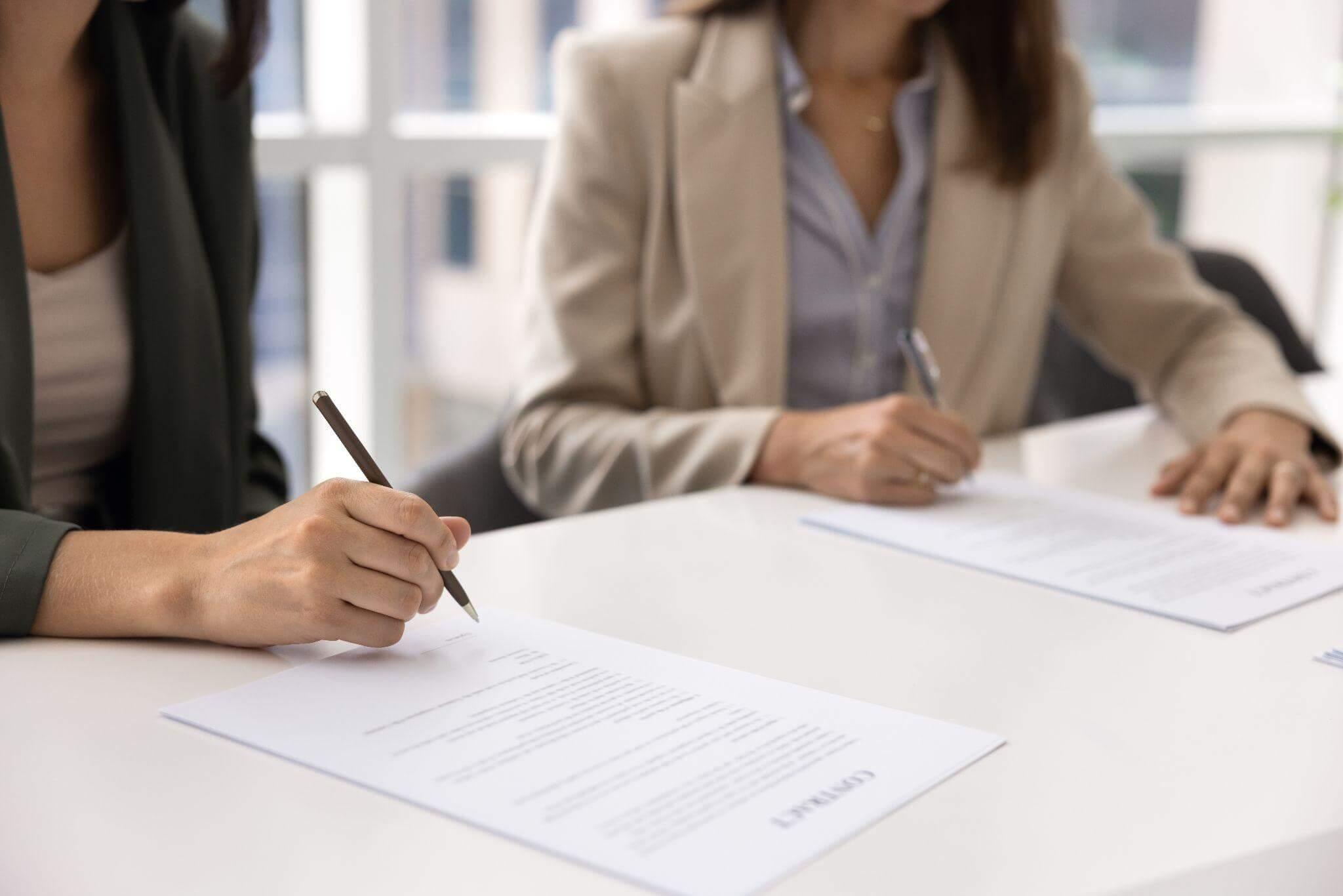 two women sitting at a table signing papers