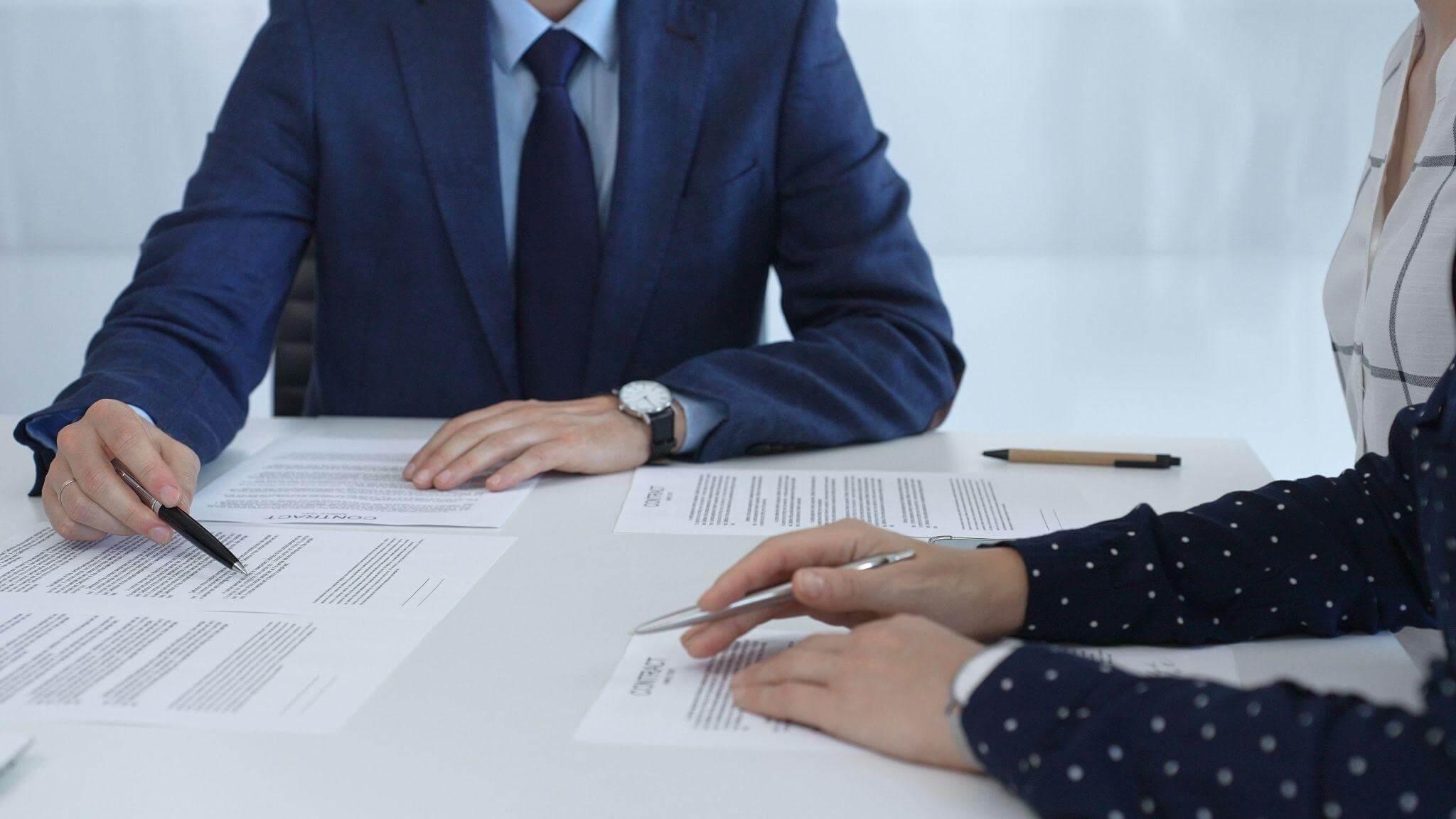 two people sitting at a table with papers and pen