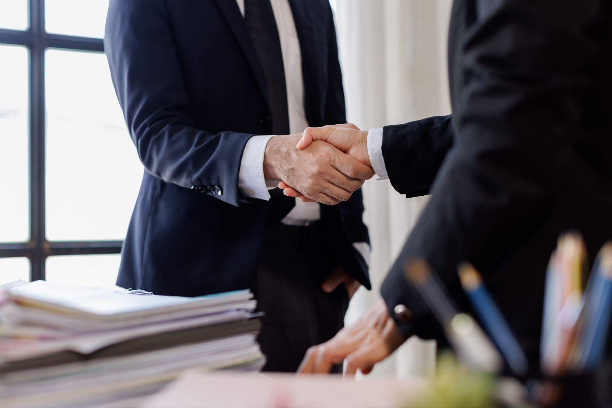 two men in suits shaking hands over a desk